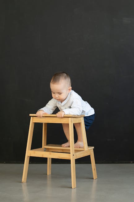 pexels-photo-32842413-32842413 A baby in a white shirt exploring a wooden stool against a black background indoors.