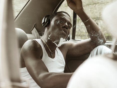 A young man in a car, wearing headphones and inhaling smoke, exudes a calm, introspective mood.