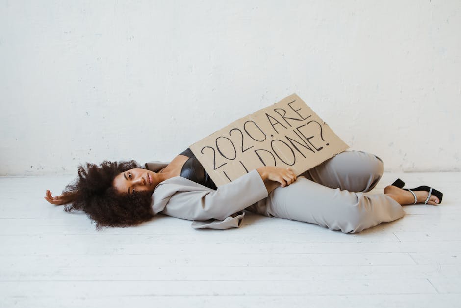 pexels-photo-6024587-6024587 Exhausted woman holding a sign expressing 2020 burnout, lying indoors on a wooden floor.